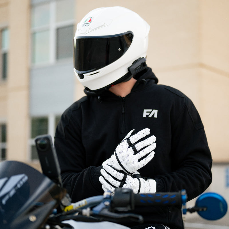 Person wearing a white helmet and black jacket with 'FA' logo, standing next to a motorcycle.
